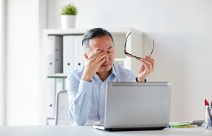 A man rubs his tired eyes while working on the computer
